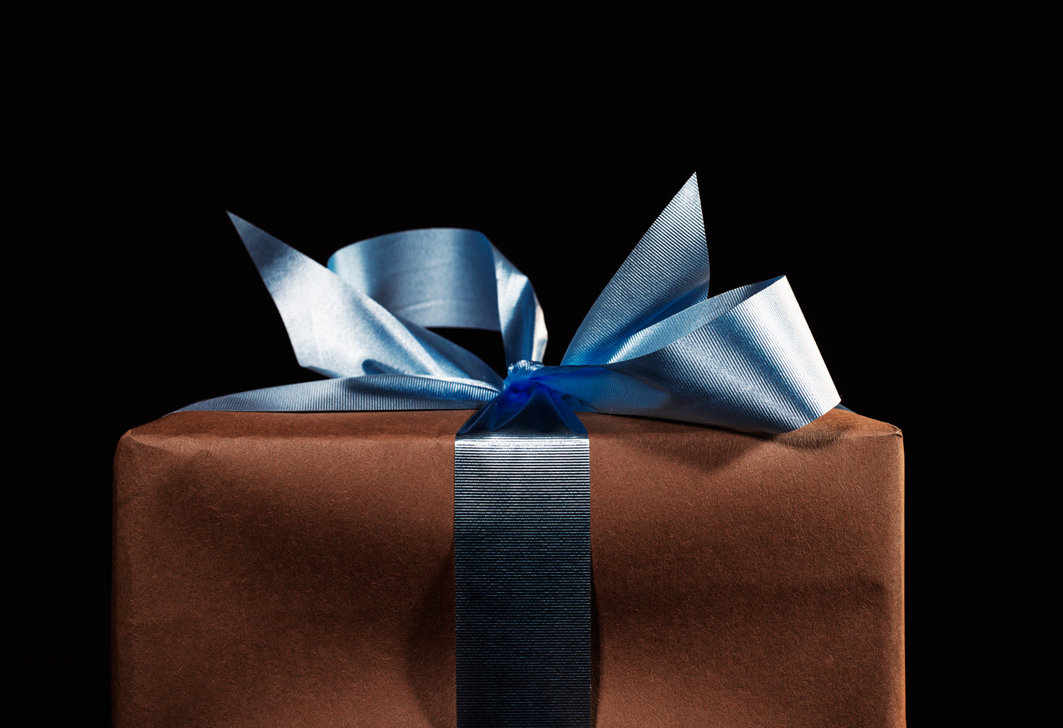 Brown gift box wrapped with a shiny blue ribbon bow on black background